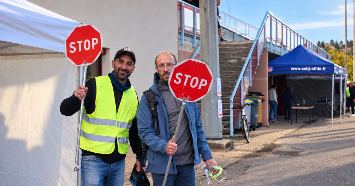 Deux bénévoles du Berjatrail tenant des panneaux STOP devant les installations du CSBJ Athlétisme